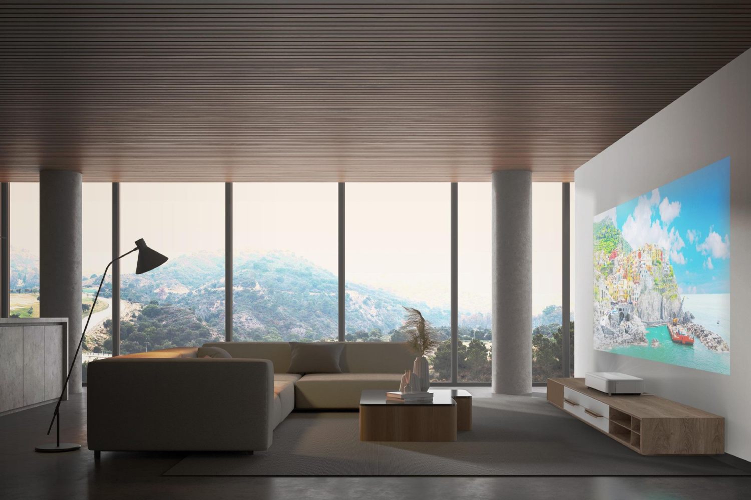 Vidéoprojecteur Epson Lifestudio Grand Plus EH-LS970W en finition blanche posé sur meuble TV bois dans un salon contemporain avec baies vitrées projetant une image lumineuse de village méditerranéen coloré sur mur blanc en plein jour