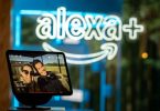 Écran connecté Amazon Echo Show affichant une photo de vacances devant une enseigne lumineuse néon bleue Alexa+, illustrant l'arrivée de l'assistant IA générative Alexa+ sur l'écosystème Fire TV en France et en Europe en 2026