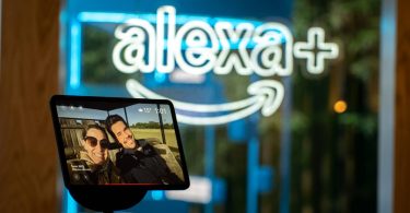 Écran connecté Amazon Echo Show affichant une photo de vacances devant une enseigne lumineuse néon bleue Alexa+, illustrant l'arrivée de l'assistant IA générative Alexa+ sur l'écosystème Fire TV en France et en Europe en 2026
