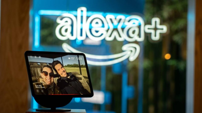 Écran connecté Amazon Echo Show affichant une photo de vacances devant une enseigne lumineuse néon bleue Alexa+, illustrant l'arrivée de l'assistant IA générative Alexa+ sur l'écosystème Fire TV en France et en Europe en 2026