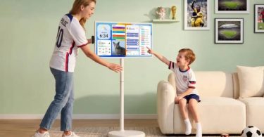 Apolosign Smart Portable TV Gen 2 32 pouces 4K sur pied à roulettes, mère en maillot équipe USA foot et enfant interagissant avec l'interface dashboard tactile dans salon contemporain mur vert, photos foot encadrées Coupe du Monde 2026 et ballon de football