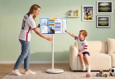 Apolosign Smart Portable TV Gen 2 32 pouces 4K sur pied à roulettes, mère en maillot équipe USA foot et enfant interagissant avec l'interface dashboard tactile dans salon contemporain mur vert, photos foot encadrées Coupe du Monde 2026 et ballon de football