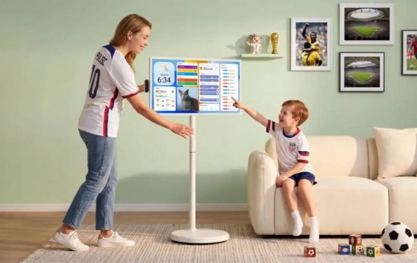 Apolosign Smart Portable TV Gen 2 32 pouces 4K sur pied à roulettes, mère en maillot équipe USA foot et enfant interagissant avec l'interface dashboard tactile dans salon contemporain mur vert, photos foot encadrées Coupe du Monde 2026 et ballon de football