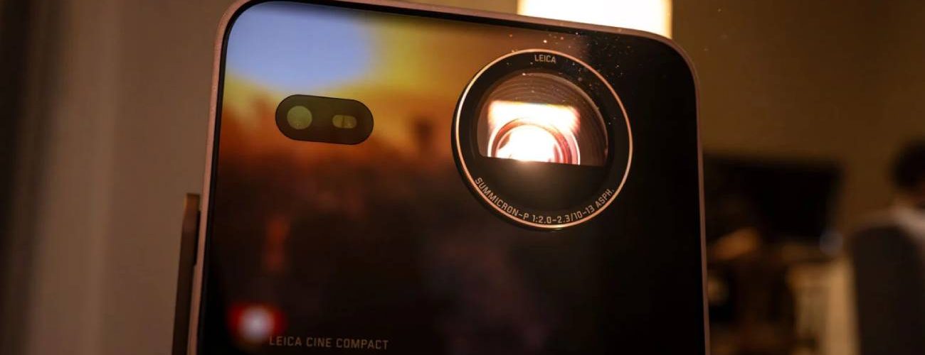 Vidéoprojecteur Leica Cine Compact 1 en boîtier aluminium noir, objectif Leica Summicron éclairé en rouge par la source triple laser RGB, posé sur un guéridon près d'une bougie dans une ambiance salon tamisée