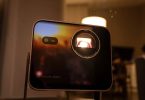 Vidéoprojecteur Leica Cine Compact 1 en boîtier aluminium noir, objectif Leica Summicron éclairé en rouge par la source triple laser RGB, posé sur un guéridon près d'une bougie dans une ambiance salon tamisée