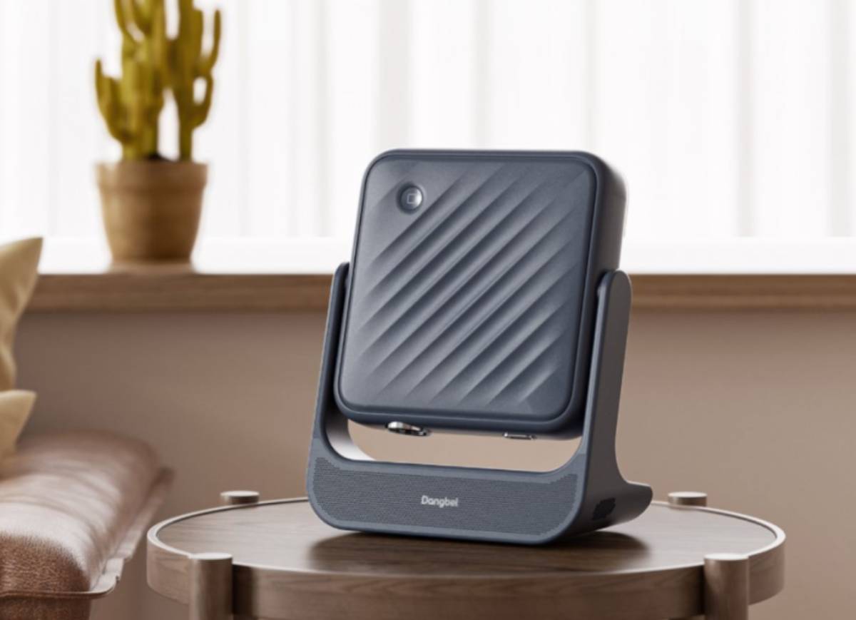 Vidéoprojecteur portable laser Dangbei RX10 gris anthracite posé sur une table basse ronde en bois, bloc optique redressé vers le haut dans son arceau cardan pour une projection au plafond, salon lumineux avec cactus et canapé en cuir