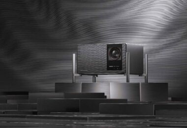 Projecteur 4K XGIMI TITAN Noir Max à triple laser RGB et double iris, badge IMAX Enhanced et grille audio Harman Kardon, posé sur un socle métallique dans un décor sombre à stries lumineuses.
