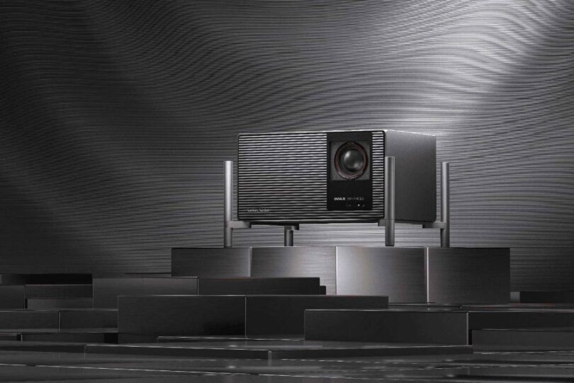 Projecteur 4K XGIMI TITAN Noir Max à triple laser RGB et double iris, badge IMAX Enhanced et grille audio Harman Kardon, posé sur un socle métallique dans un décor sombre à stries lumineuses.