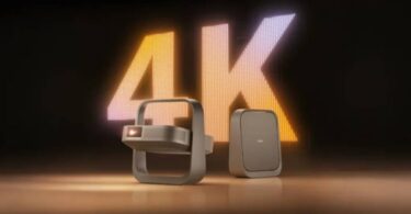 Projecteur portable XGIMI Z9X 4K High Brightness Edition au design cadre-poignée cardan, finition bronze, posé à côté de son bloc d'alimentation devant un mur LED géant affichant 4K en lettres lumineuses orange et blanches