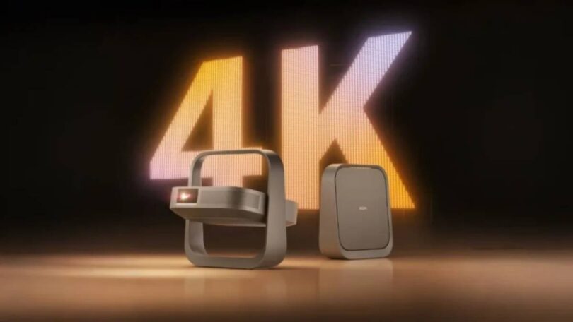 Projecteur portable XGIMI Z9X 4K High Brightness Edition au design cadre-poignée cardan, finition bronze, posé à côté de son bloc d'alimentation devant un mur LED géant affichant 4K en lettres lumineuses orange et blanches