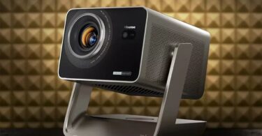 Projecteur Hisense de la gamme C3 triple laser 4K, finition gris titane sur support à cardan, objectif zoom 1,6x avec iris et marquage Tuned by Devialet, devant un mur acoustique doré