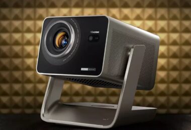 Projecteur Hisense de la gamme C3 triple laser 4K, finition gris titane sur support à cardan, objectif zoom 1,6x avec iris et marquage Tuned by Devialet, devant un mur acoustique doré