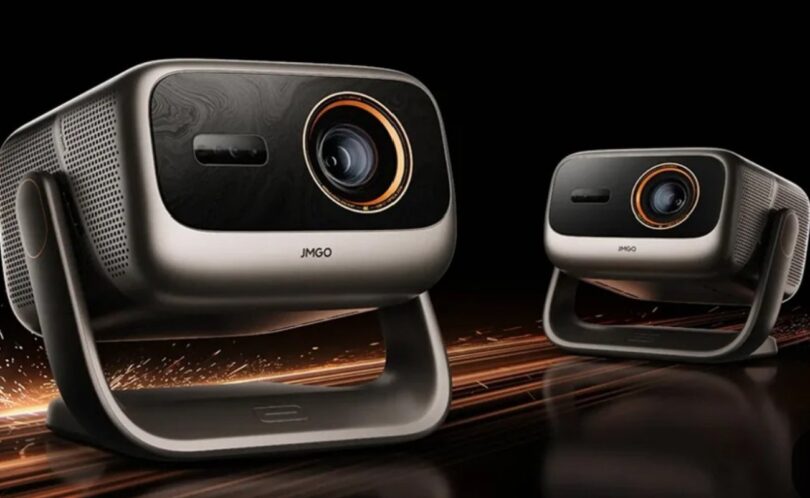Deux vidéoprojecteurs JMGO Iris triple laser 4K 120 Hz, coque argent champagne, façade noire, objectif cerclé d'orange et rotule en U, sur fond noir avec étincelles cuivrées